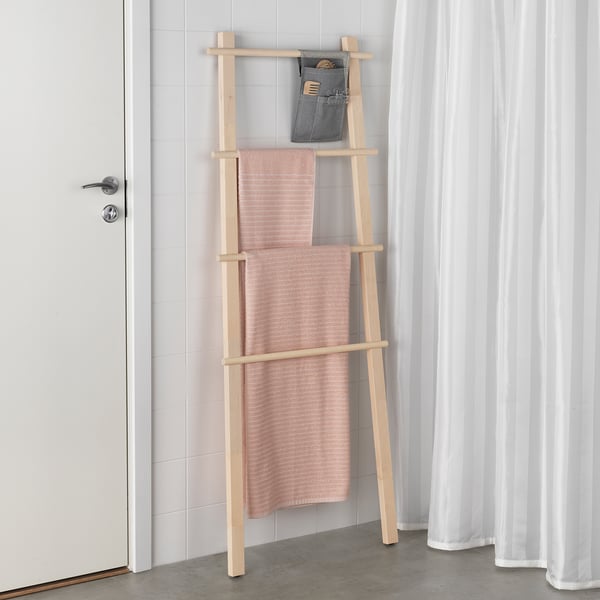Wooden towel rack in birch holds pink towels, beside door with silver handle; gray pouch above for storage.
