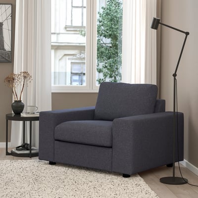 Modern grey armchair in living room. Next to side table with vase and lamp. Medium size compared to surroundings.