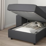 Modern grey sofa with raised seat revealing storage space with blankets inside.