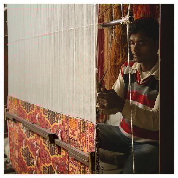 Man weaving colorful rug on loom.