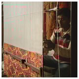 Man weaving colorful rug on loom.