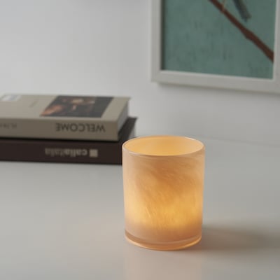 Illuminated glass candle holder on table, near books.
