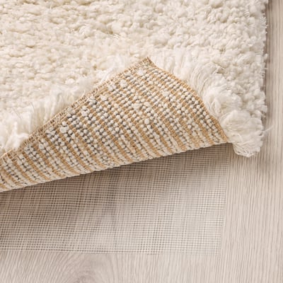 Fluffy white rug with textured yarn, shown with anti-slip mesh underlay.