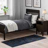 Small, dark bedroom with a neatly made bed, dark wood furniture, and a patterned area rug on the floor.