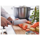 Person preparing vegetables with a VÖRDA knife, which has blade indentations to prevent sticking.