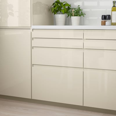 Modern kitchen with beige glossy drawers and potted herbs on top.