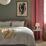 Een gezellige slaapkamer met een ÅKERFIBBLA geruit dekbedovertrek in wit en zwart op een groot bed, aangevuld met rode gordijnen en een ingelijste kunst aan de muur.