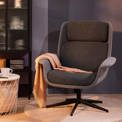 Gezellige ÄLEBY grijze fauteuil met zwart onderstel, gedrapeerde deken, op rond vloerkleed bij witte bijzettafel met kopje.