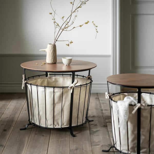 Twee rustieke tafels met opbergtassen. De ene heeft een vaas en schaal. Houten vloer, groene muur.