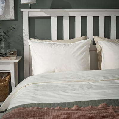 Bed met witte kussens, groene muur, lamp, plant, mand.