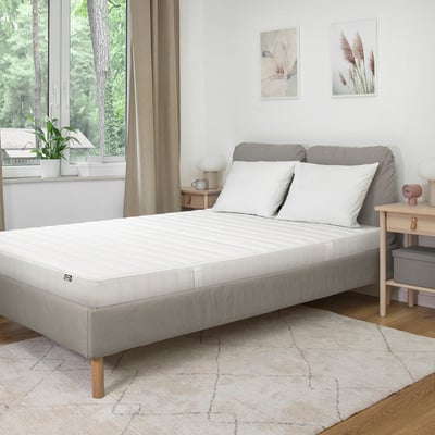 Moderne minimalistische slaapkamer met witte matras, grijs bedframe, houten vloeren, vloerkleed, nachtkastje, lamp, twee wandfoto's, net bed, groot raam.