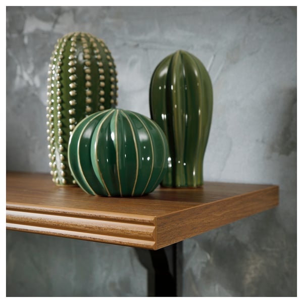 Drie groene keramische cactussen op een houten plank tegen een grijze muur. Verschillende vormen en texturen.