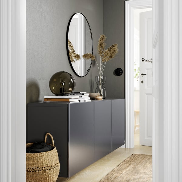 Moderne entree met donkergrijs BESTÅ meubel, ronde spiegel, gedroogde planten, boeken en rieten mand.
