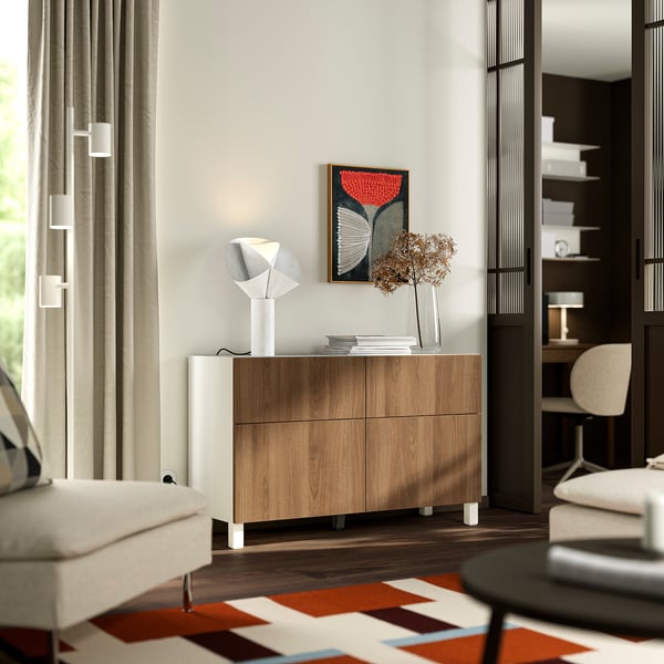 Moderne minimalistische kamer met BESTÅ dressoir, lamp, gedroogde bloemen, vloerkleed, fauteuil, raam en boekenplank.