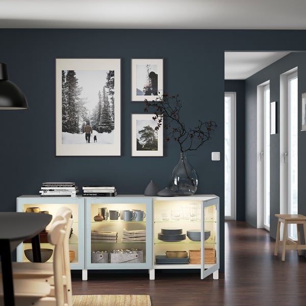 Moderne eetkamer met BESTÅ dressoir. Het uitstallen van schalen, vazen en boeken. Kunst aan de muur en plantdecoratie. Zachte verlichting en houten vloer.