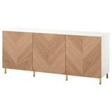 Een wit en houten dressoir met gouden poten. Het heeft drie houten deuren met een chevronpatroon en veel opbergruimte.