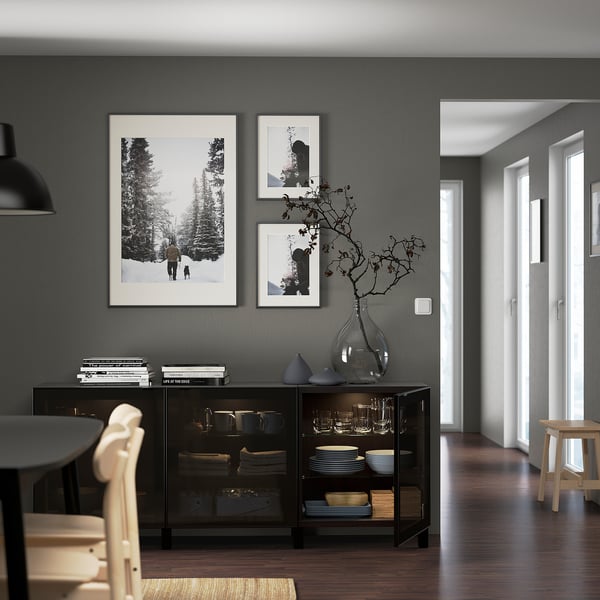 Moderne woonkamer met verstelbare, aan de muur gemonteerde BESTÅ opbergkast met glazen deuren met borden en een decoratieve vaas, naast ingelijste kunst.