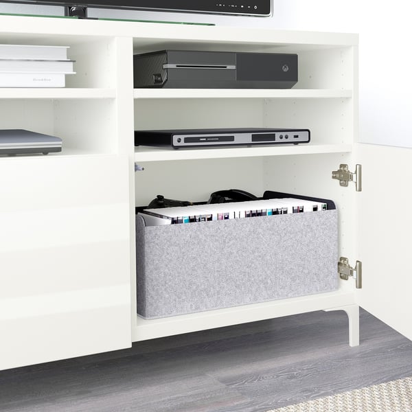Wit BESTÅ tv-meubel met planken voor het opbergen van elektronica, waaronder een dvd-speler en een gameconsole. Zachtsluitende deuren verbergen georganiseerde mediakabels.