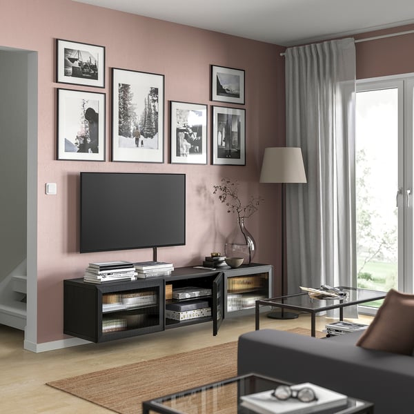 Woonkamer met tv op moderne zwarte BESTÅ-standaard, roze muren, grijze gordijnen, ingelijste foto's, lamp en glazen salontafel.