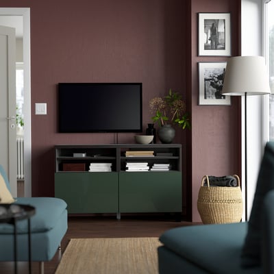 Moderne woonkamer met BESTÅ groen tv-meubel, boeken en inrichting. Donkerpaarse muur, blauwe stoelen en rieten mand.