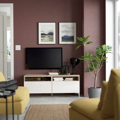 Moderne woonkamer met BESTÅ tv-meubel, flatscreen, gele fauteuils, plant, bergfoto's, houten accenten en opbergruimte.