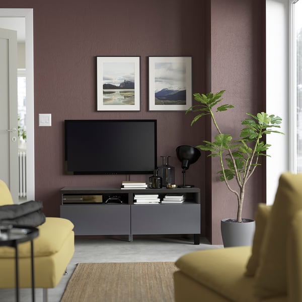 Moderne woonkamer met donkerpaarse muur, BESTÅ tv-meubel, flatscreen-tv, gele stoelen, natuurfoto's en potplant.