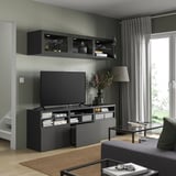 Moderne woonkamer met grijs BESTÅ tv-meubel, flatscreen tv, wandkasten, donkere houten vloer en groot raam.
