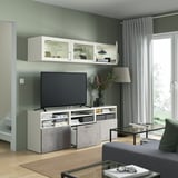 Moderne woonkamer met BESTÅ tv-meubel, verstelbare planken en wandkasten. Flatscreen-tv, inrichting en lamp in de buurt. Glazen salontafel aan de voorkant.