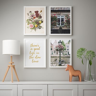 Wandgalerij met bloemenprints en citaatlijst, naast een lamp en houten paard op tafel.