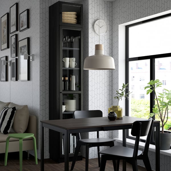 Moderne eetkamer met BILLY boekenkast, zwarte stoelen, houten tafel, groot licht, kunst aan de muur, klok en uitzicht op het raam van het groen.