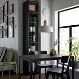 Moderne eetkamer met BILLY boekenkast, zwarte stoelen, houten tafel, groot licht, kunst aan de muur, klok en uitzicht op het raam van het groen.