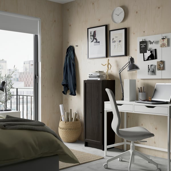 Moderne slaapkamer met BILLY boekenkast, stoel en bureau. Uitzicht op de stad vanuit het raam, artistieke prints en een georganiseerd bureau met benodigdheden.