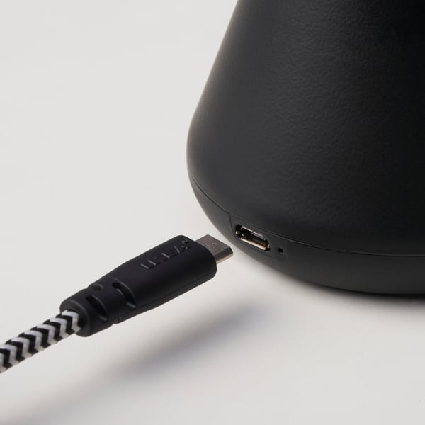 Zwarte luidspreker met usb-c-ingang, aangesloten via usb-kabel, met oplaadbare functie.