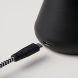 Zwarte luidspreker met usb-c-ingang, aangesloten via usb-kabel, met oplaadbare functie.