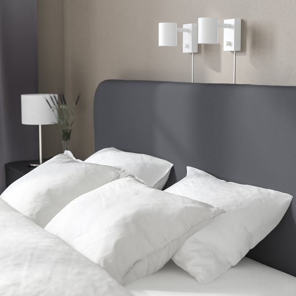 Een minimalistische slaapkamer met een grijs bed, witte kussens en een moderne lamp.