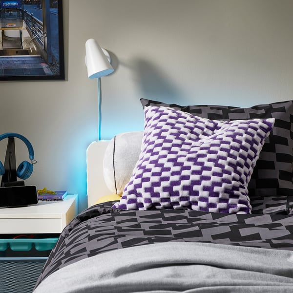 Modern bed met BLÅSKATA geometrisch dekbed, zwart/grijs/witte kussens, grijs beddengoed, nachtkastje, lamp en koptelefoon.