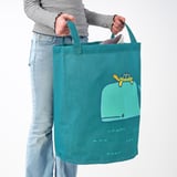 Persoon die een turquoise draagtas met groen walvisontwerp vasthoudt en deze aan de handvatten draagt.