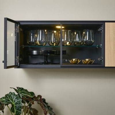 Glazen wandkast met tweevoudige eiken deuren, met glaswerk en gouden schalen. Binnenverlichting zet items in de schijnwerpers.