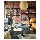 Industriële woonkamer: bakstenen muur, trap, meubels. Zwarte metalen planken, grijze poef, bruin lederen stoel, hanglamp.