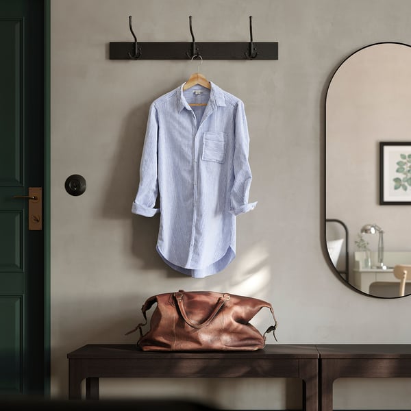 Entreeopstelling met BUMERANG houten hanger met een blauw gestreept shirt. Donkerbruine leren tas en ronde spiegel in de buurt. Zwarte kapstok boven.