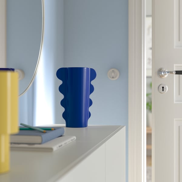 Helderblauwe golvende DOFTBRÄKEN vaas op plank, bij witte deur.