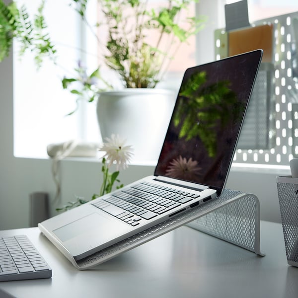 Zilveren laptopstandaard met mesh organizer en plant.