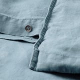 Close-up van een blauwgrijs linnen dekbedovertrek met knoopsluiting, met de nadruk op textuur en detail.