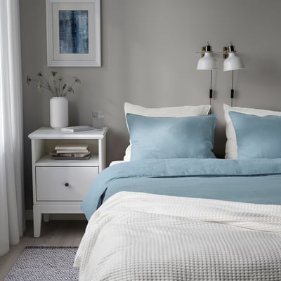 Gezellige slaapkamer met dubbele lampen, vaas, boeken en glas. Blauw bed, 2 kussens, warme deken, kunst, gordijn. Bed groter dan nachtkastje.