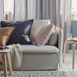 Een knusse grijze bank met meerdere kussens en dekens. Zacht textiel, gevarieerde texturen en een warme inrichting creëren een gastvrije leefruimte.