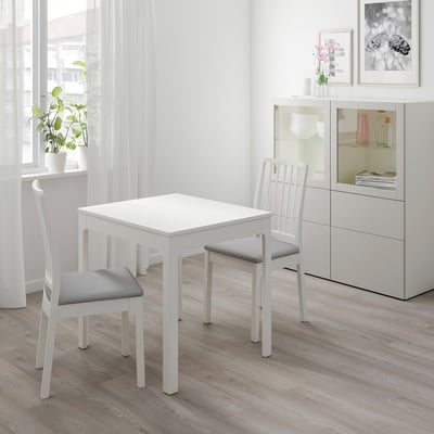 Kleine witte eethoek met vierkante tafel en twee stoelen met kussens, ideaal voor gezellige ruimtes.