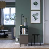 Modern grijs opbergmeubel met planken, lades en een cactus, naast een deur in een lichte kamer.