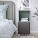 Modern nachtkastje met EKET grijze kast, boeken, groen hoofdeinde en cactus.