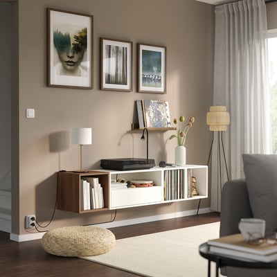 Moderne woonkamer met EKET plank, platenspeler, boeken, lamp en kunst. Grijze bank, staande lamp en vitrage bij het raam.