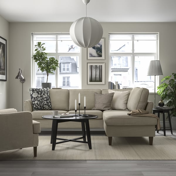 Moderne woonkamer met EKHOLMA beige bank, salontafel, kussens. Grote ramen, planten, hanglamp.